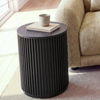 Ayla Fluted 40cm Round Side Table Black beside the arm of a light sofa, with a cup on a linen book, in a sunlit living room