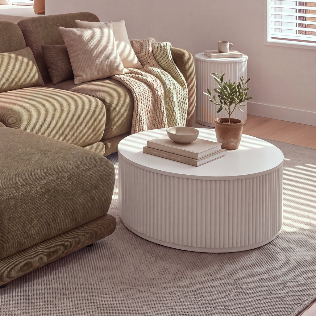 Ayla Fluted 40cm Round Side Table White behind the corner of a sofa with a matching fluted coffee table in front, in striped sunlight
