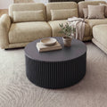 Ayla Fluted 90cm Round Coffee Table Black in front of a modular sofa on a rug, with a bowl on stacked books and a potted olive tree