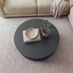 Ayla Fluted 90cm Round Coffee Table Black seen from above on a rug in front of a sofa, with a bowl on books and a small potted olive tree