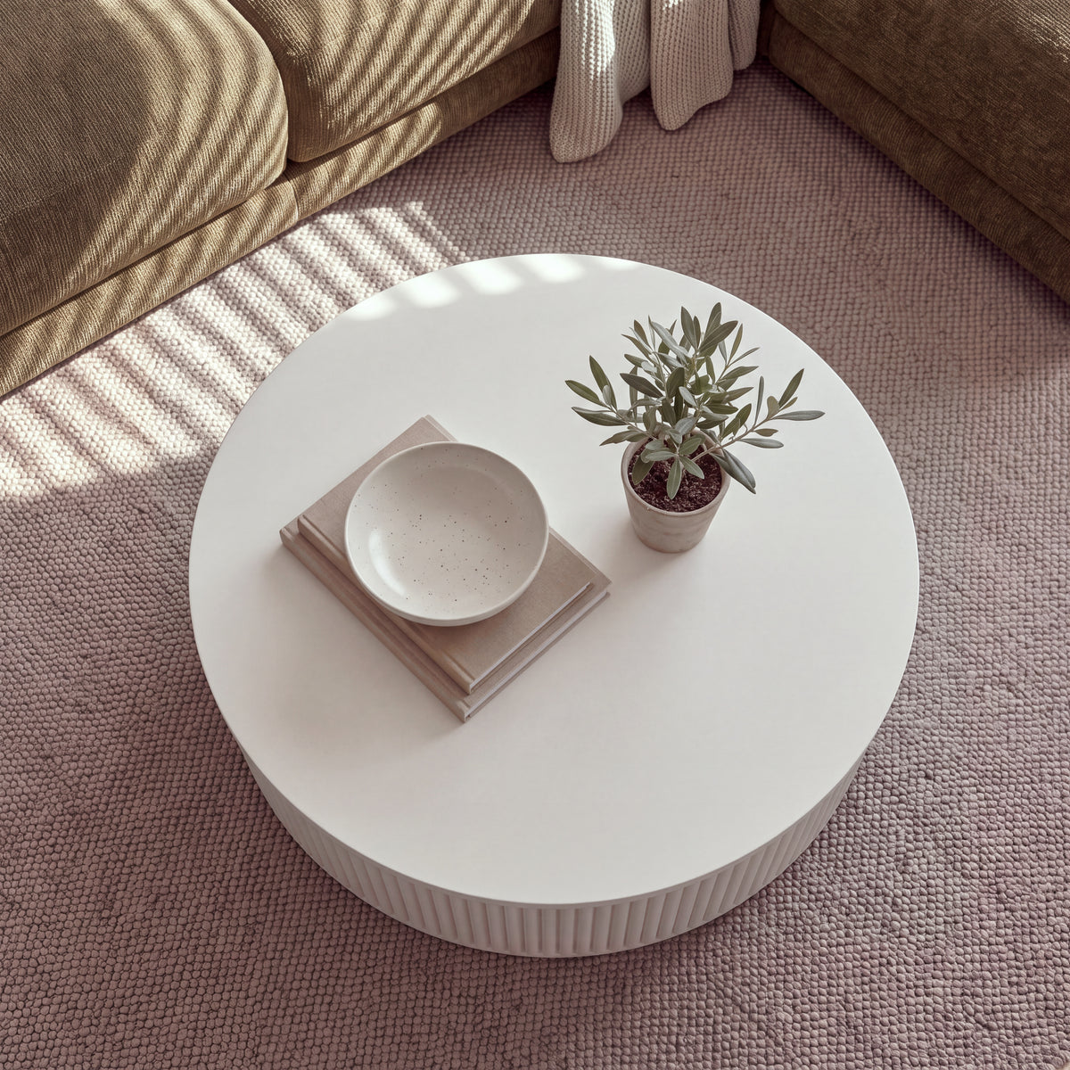 Ayla Fluted 90cm Round Coffee Table White seen from above on a rug, with a bowl on books and a small potted olive tree