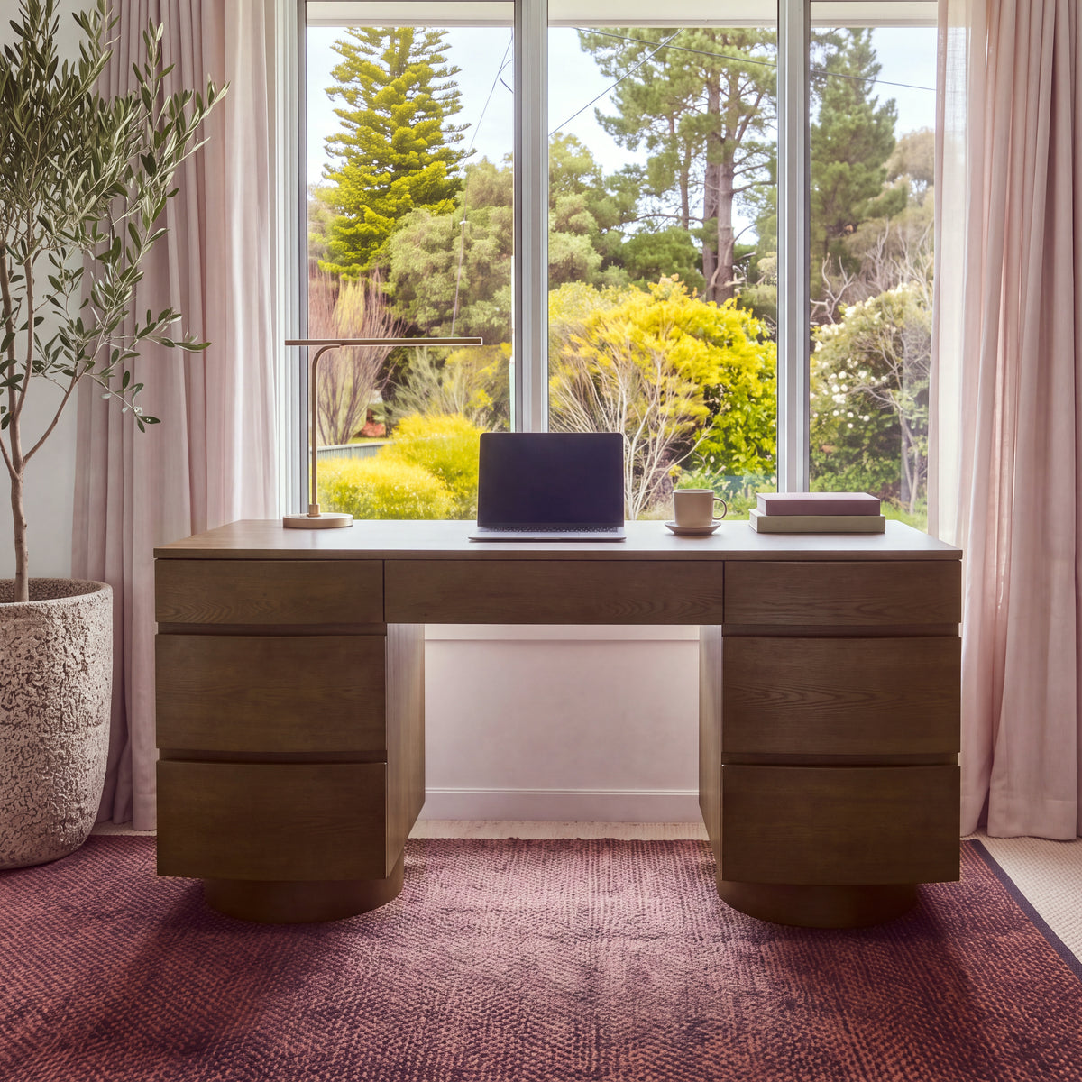 Dorit 172cm 7 Drawer Home Office Desk Walnut, front view against a window with sheer pink curtains