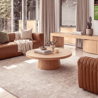 Erina 110cm Round Coffee Table Natural Oak, in a living room beside a leather sofa, three-quarter view