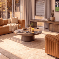 Erina 110cm Round Coffee Table Natural Walnut, in a living room beside a leather sofa, three-quarter view