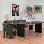 Eve 240cm Oval Dining Table Black with an olive velvet armchair at one end and a matching bench behind, shown with a reeded sideboard