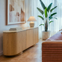 Hera 180cm Sideboard Buffet Table Natural, three-quarter view beside a leather sofa and an indoor plant