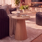 Hera 55cm Round Side Table Natural, styled with a mug and books beside a sofa