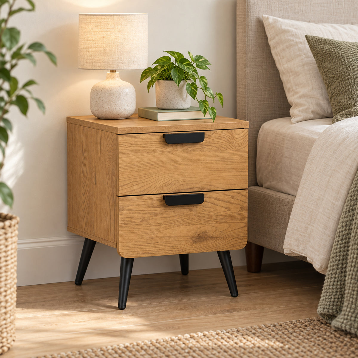 Jinan 2 Drawer Bedside Table Oak, beside a bed with a table lamp on top