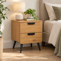 Jinan 2 Drawer Bedside Table Oak, beside a bed with a table lamp on top