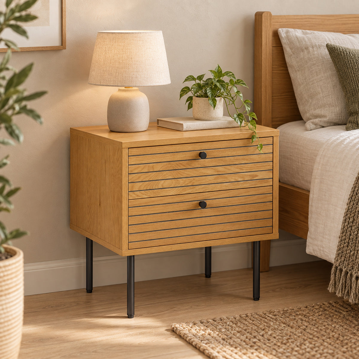 Line 2 Drawer Bedside Table Oak and Black, beside a bed with a table lamp on top
