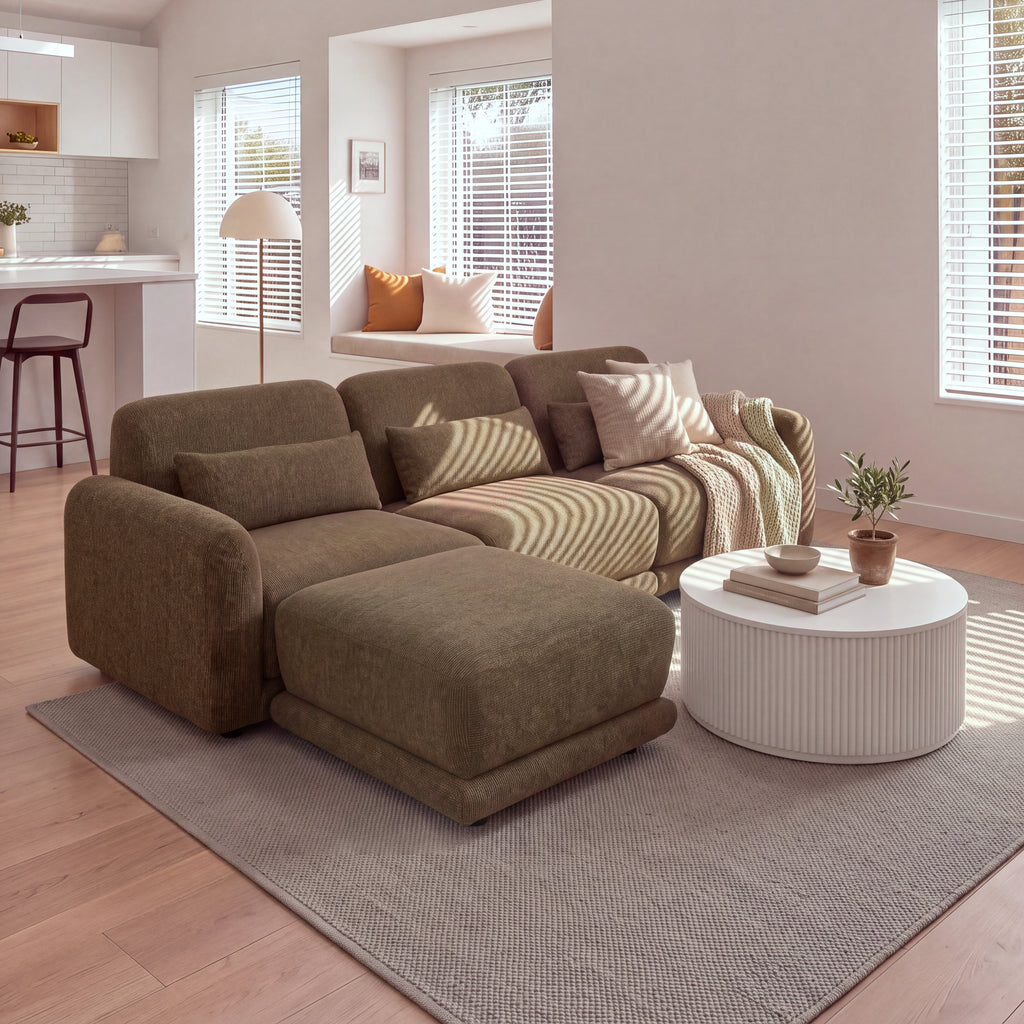 Paulie 270cm 3 Seater Modular Sofa with Ottoman Chocolate with the ottoman pushed against the left seat as a chaise, beside a round white fluted coffee table in a sunlit living room
