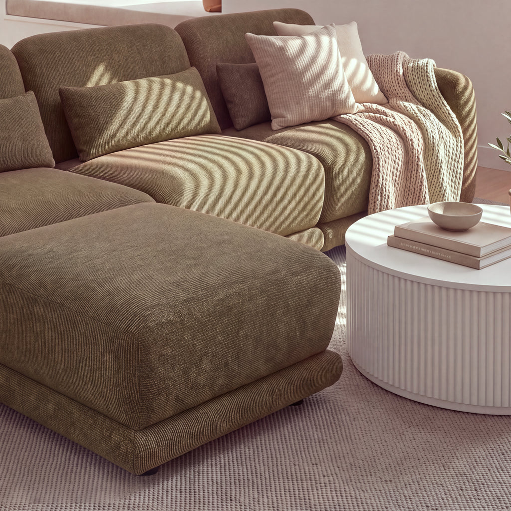 Paulie 270cm 3 Seater Modular Sofa with Ottoman Chocolate, close-up of the ottoman and seat cushions in striped sunlight beside a white fluted coffee table