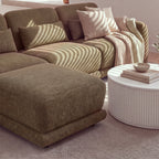 Paulie 270cm 3 Seater Modular Sofa with Ottoman Chocolate, close-up of the ottoman and seat cushions in striped sunlight beside a white fluted coffee table