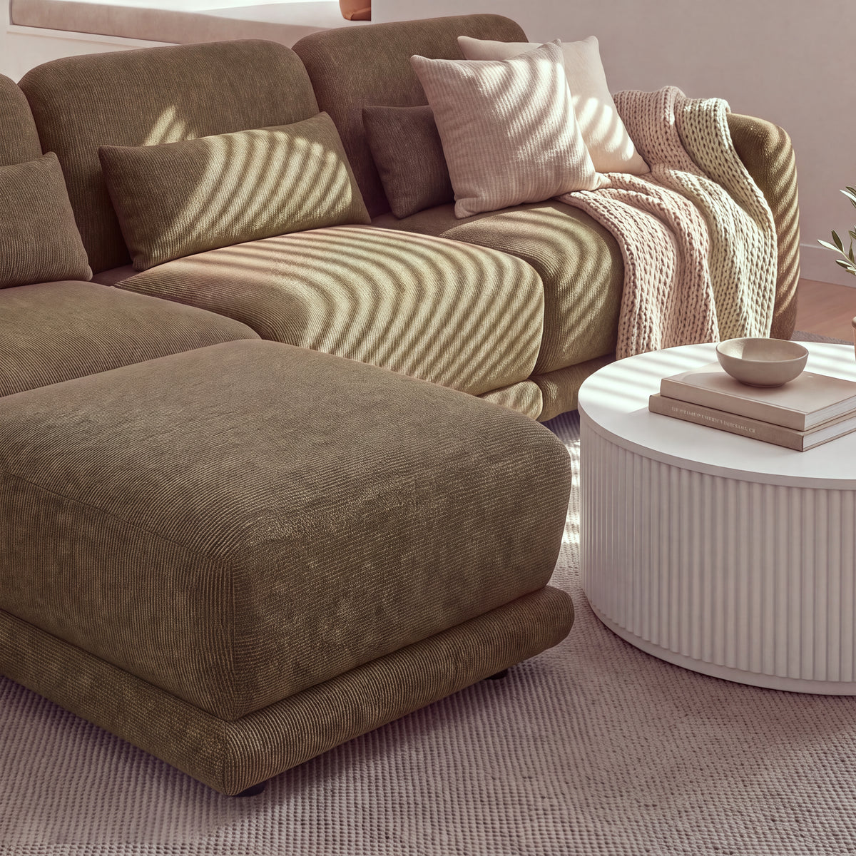 Paulie 270cm 3 Seater Modular Sofa with Ottoman Chocolate, close-up of the ottoman and seat cushions in striped sunlight beside a white fluted coffee table