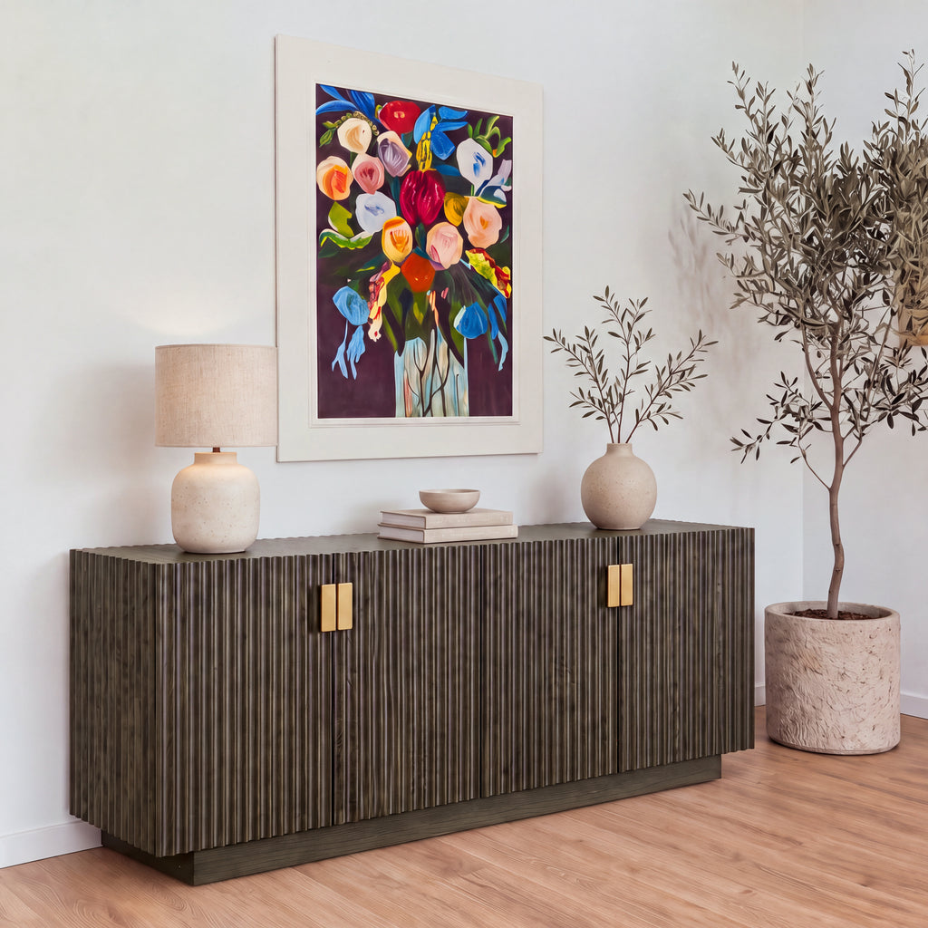 Sloane 180cm Buffet Table Storage Cabinet Grey Oak under a large floral painting, with a table lamp, books and a vase on top and an olive tree beside it