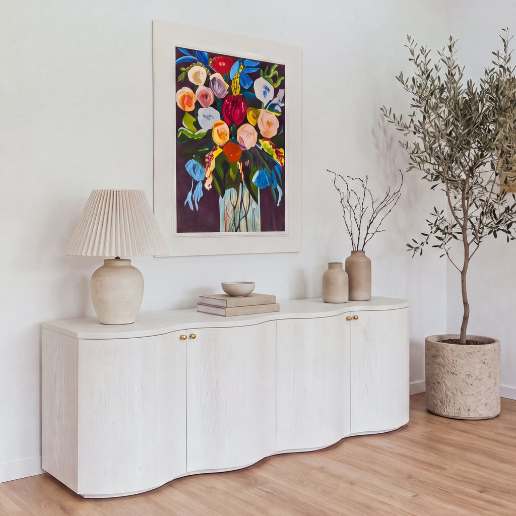 Wave white buffet under a floral painting in a bright dining room, front three-quarter view