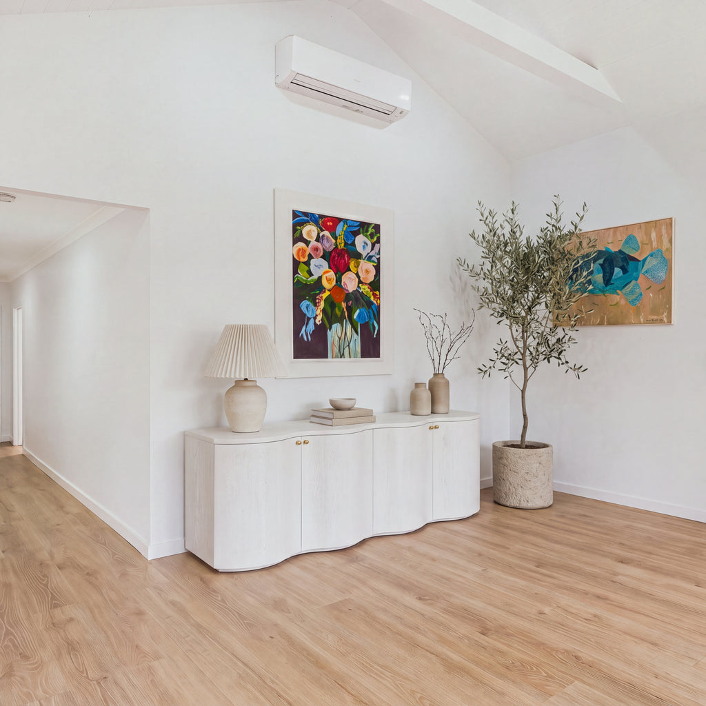 Wave white buffet against a dining room art wall beside an olive tree, wide view